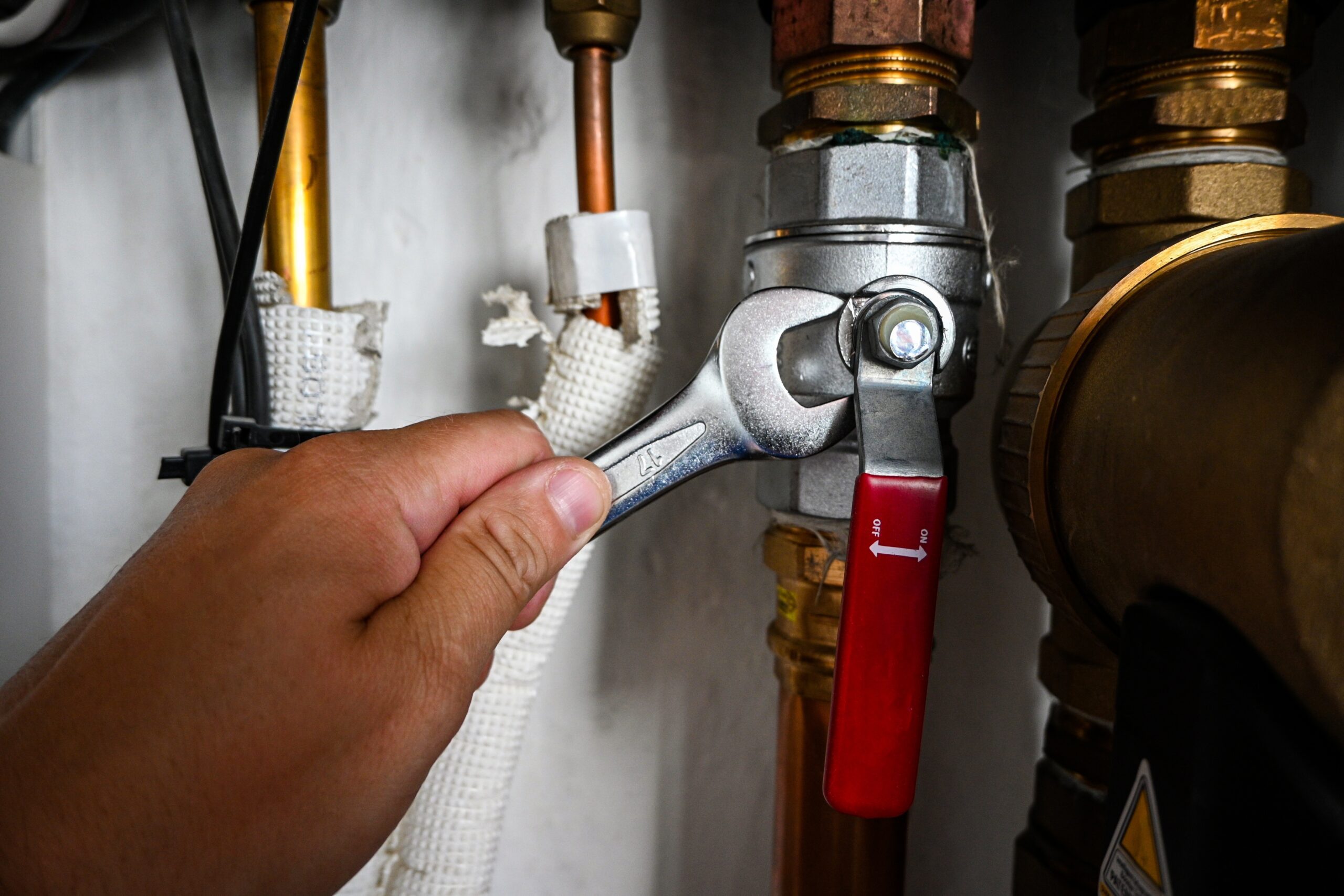 Plumber,Is,Tightening,A,Nut,On,A,Water,Heater,Pipe A hand uses a wrench to tighten a metal valve connected to copper pipes and plumbing fittings.